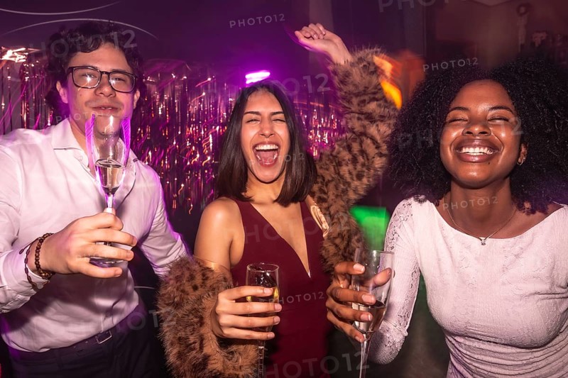 Happy diverse friends clinking champagne in a vibrant nightclub, dancing under dynamic lights and tinsel, celebrating togetherness, joy, and festive weekend nightlife energy