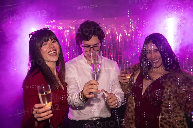 Friends cheering and having fun while celebrating a party with champagne and bubbles, experiencing joy and happiness in a vibrant night club atmosphere with purple lighting