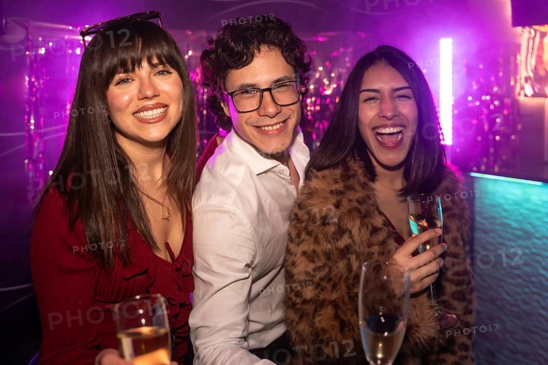 Three diverse young friends celebrating and having fun together at a vibrant nightclub, holding champagne glasses and laughing under purple neon lights