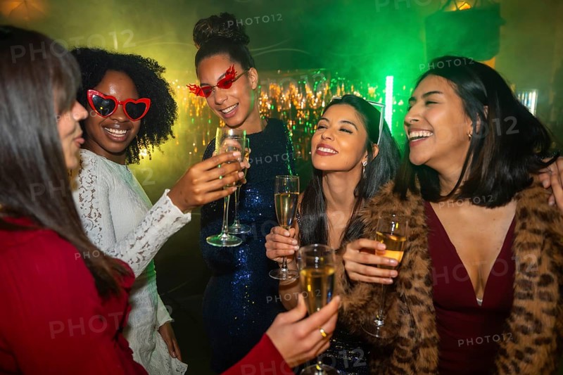Diverse group of young women friends happily toasting with champagne flutes, celebrating a special occasion together in a dynamic and festive nightlife setting with green lighting