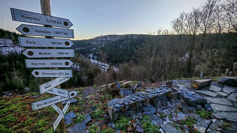 Wooden signpost at a viewpoint with views over wooded hills and valleys in winter, Franconian Forest nature park Park