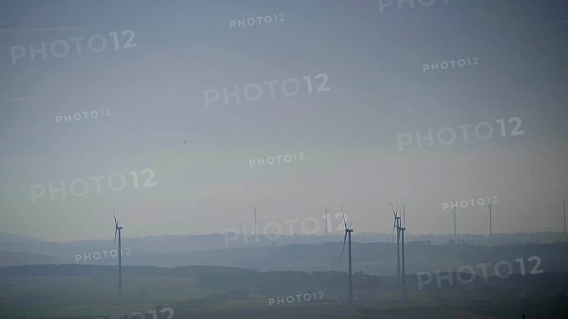 Blurred range of hills with isolated wind turbines in morning fog under blue sky, Franconian Forest nature park Park