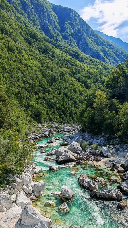 Stream flows through rocky landscape with green mountains in the background, Soca Valley, Slovenia