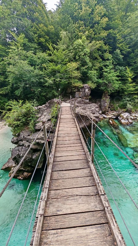 Wooden suspension bridge over green-turquoise water, surrounded by thick forest, Soca Valley, Slovenia