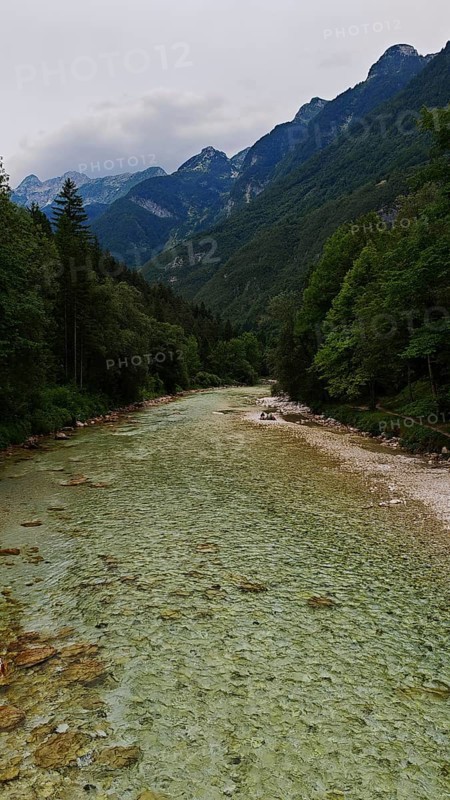 Long river with gravel bed surrounded by wooded mountains under a cloudy sky, Soca Valley, Slovenia