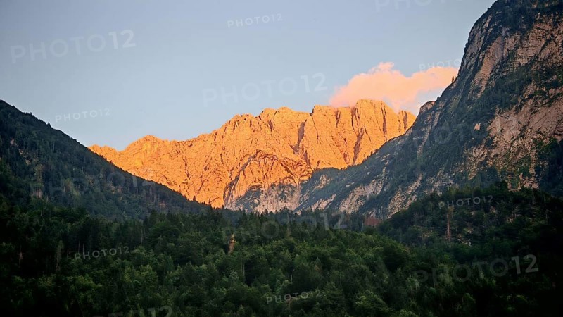 Mountains at sunset with impressively illuminated rocks and dark forest in the foreground, Slovenia