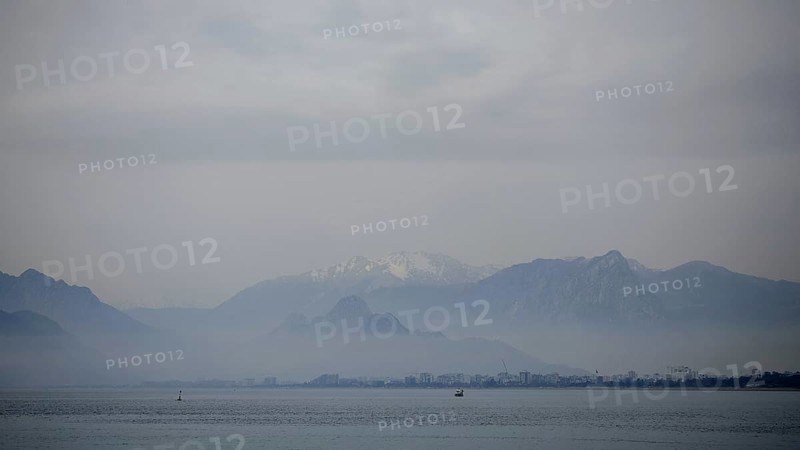 Blurred mountains and a distant city in fog over a calm sea with boats, Antalya, Turkey