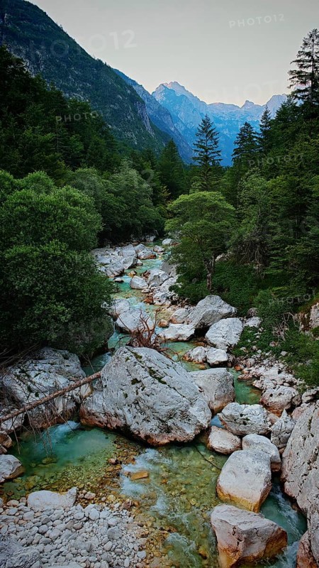 A clear mountain river surrounded by rocks and trees with mountains in the background, Soca Valley, Slovenia
