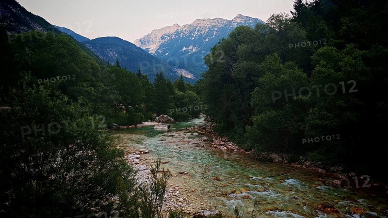 A mountain river flows through a wooded landscape with mountains in the background, Soca Valley, Slovenia