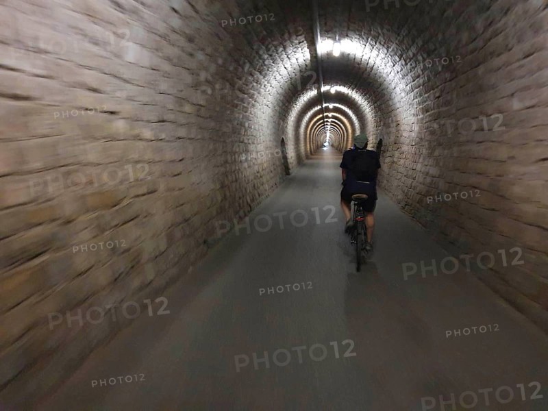 A cyclist crosses a long, illuminated stone tunnel, Slovenia
