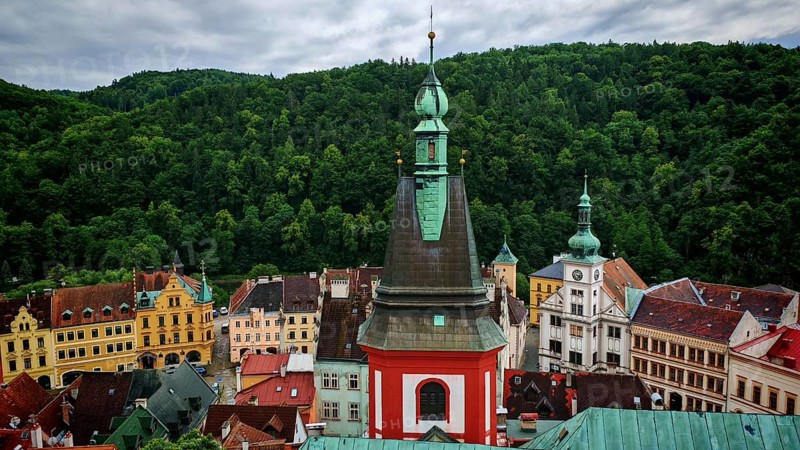 View of a town with church tower and historic buildings in front of a forest, Loket, Czech Republic