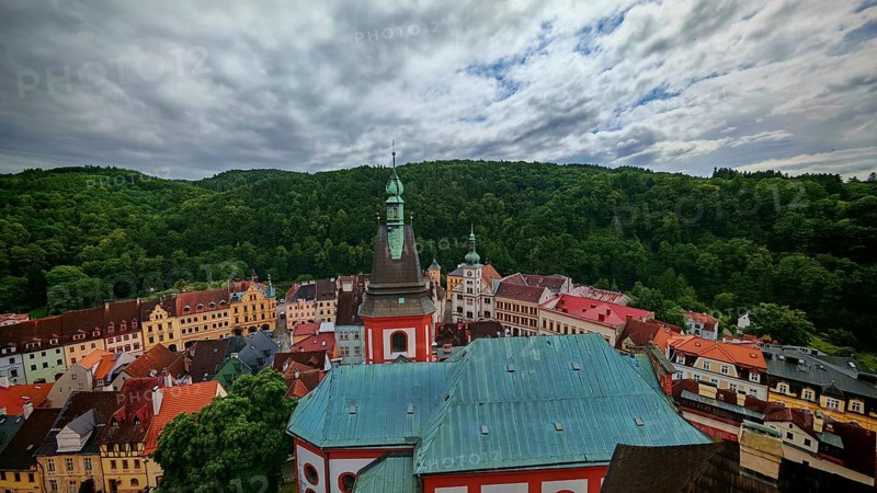 City view with church tower and historic buildings in front of wooded hills, view of Loket, Czech Republic