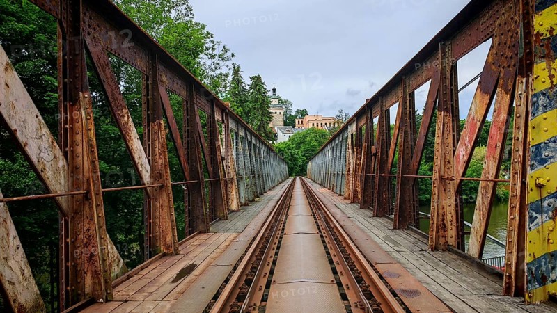 Old, rusty metal railroad bridge leads through green forests to a remote small town, Loket, Czech Republic