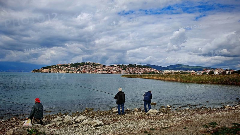 Fishermen on the shore of a lake with a view of a city in the background under cloudy sky, Ohrid, North Macedonia
