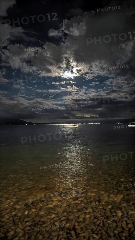 A nighttime lake panorama with reflecting moonlight and dramatic clouds in the sky, Lake Ohrid, North Macedonia