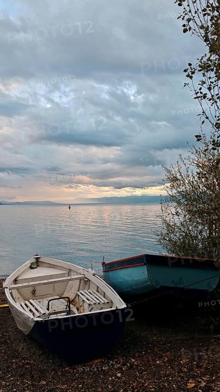 Two boats are lying on the shore of a calm lake under a cloudy evening sky, Lake Ohrid, North Macedonia