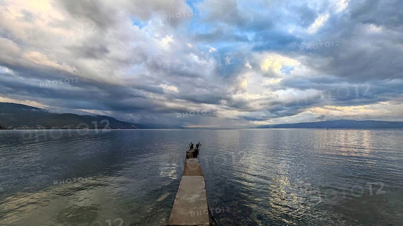 A narrow footbridge stretches out into endless water under a dramatic sky full of clouds, Lake Ohrid, North Macedonia