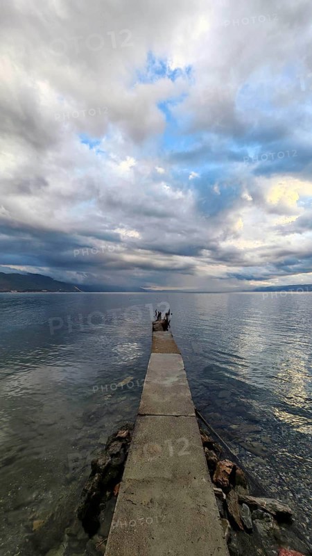 A long jetty leads into the calm sea under a cloudy sky that creates a peaceful atmosphere, Lake Ohrid, North Macedonia