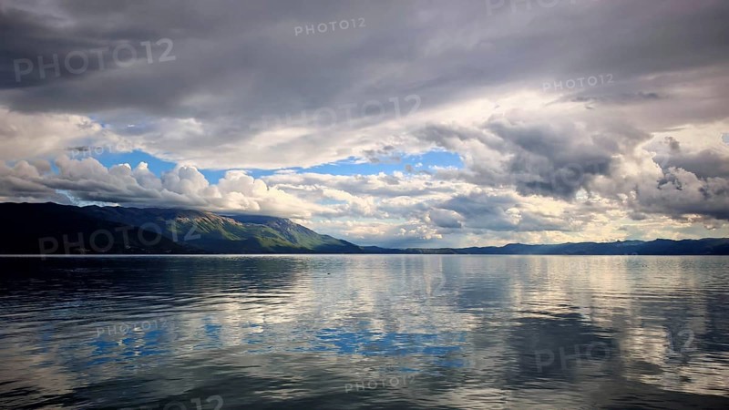 Extensive lake with reflective, dramatic clouds and calm water and mountains in the background, Lake Ohrid, North Macedonia