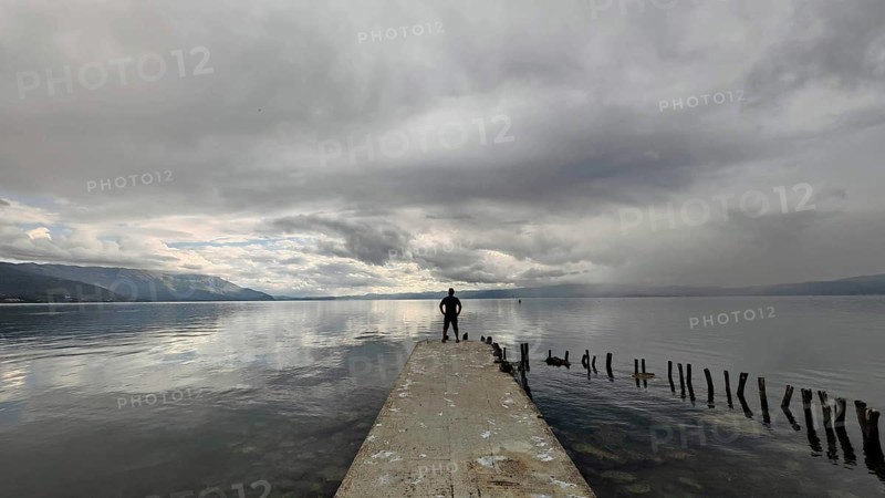 A man stands alone on a jetty that juts into a cloud-covered lake, Lake Ohrid, North Macedonia