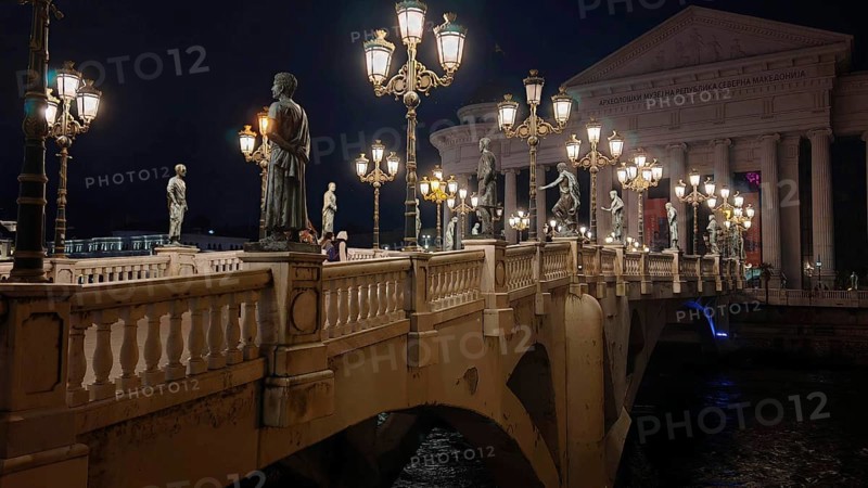 Illuminated bridge at night with statues and decorative lamps, Skopje, North Macedonia