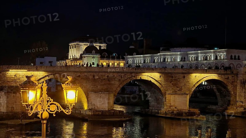 Illuminated bridge at night over a river with historic architecture, Skopje, North Macedonia