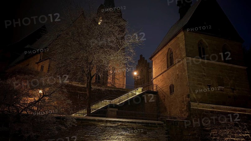 Illuminated church in the dark, surrounded by trees, conveys medieval atmosphere, view of Kronach, Frankenwald nature park Park