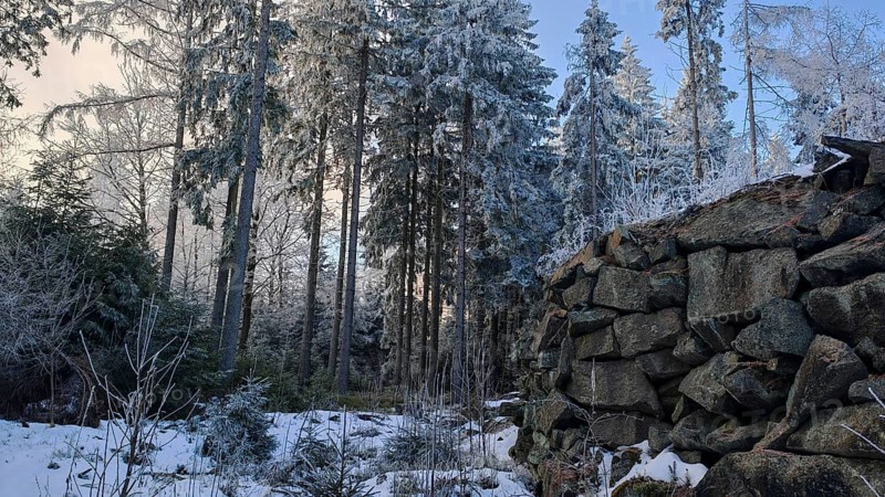 Cold winter picture with a pile of stones in the forest, old quarry surrounded by snow-covered trees and clear sky with dusk in the background, Fichtelgebirge