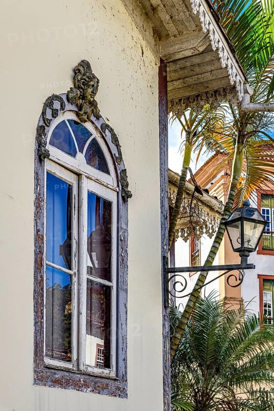 Old window decorated with a sculpture of a face and other ornaments in a historic house in the city of Ouro Preto, Ouro Preto, Minas Gerais, Brazil