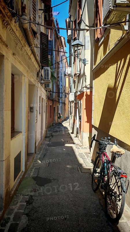A bicycle is parked in a narrow sunny alley between old buildings, Slovenia