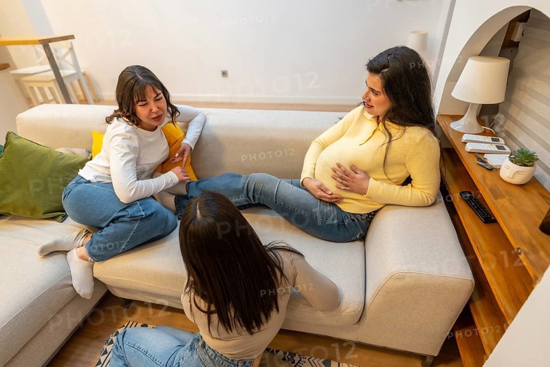 Pregnant woman resting on a sofa. Communicating with her friends. Receiving support and comfort during her pregnancy journey. Creating a warm moment of female bonding and connection in the living room