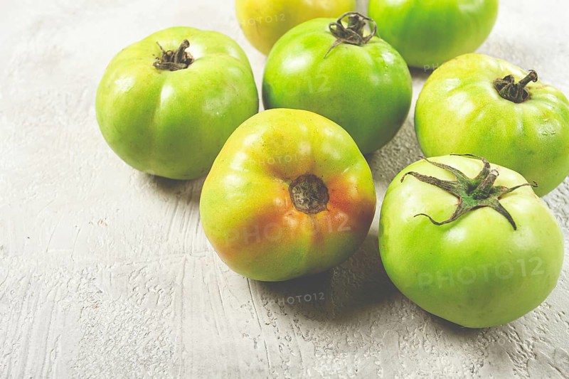 Green tomatoes scattered on the table, unripe tomatoes, raw, selective focus, no people