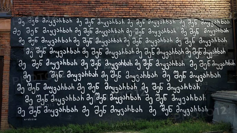 A wall that stands in white letters on a black background in McHedruli writing Ich liebe Dich, against a brick background, Georgia