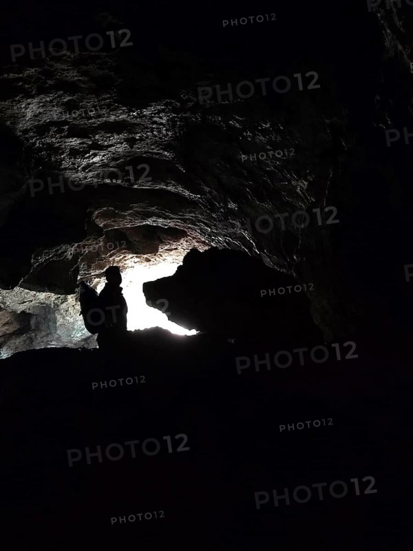 Silhouette of a person in a dark cave entrance with a ray of light from outside and a rock that looks like a big boar (aprum), Franconian Switzerland, Germany