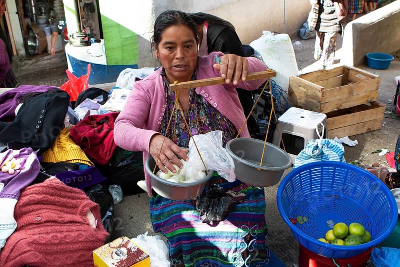 Mayan woman in traditional clothing weighs with a hand scale at the market in Sololá, Highlands, Sololá Department, Guatemala