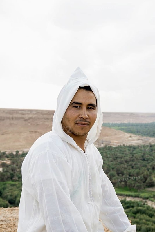 Young man and oasis in the background, near Merzouga, Meknès-Tafilalet region, Erg Chebbi, northern Sahara, Morocco