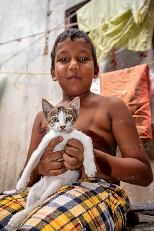 Topless boy proudly holds a cat and smiles in an interior