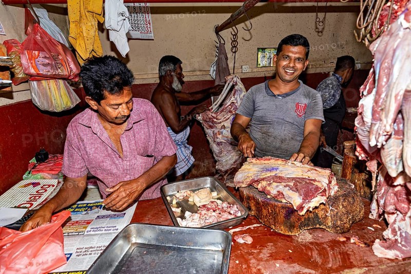 Butcher working with fresh meat, one smiles and works on a large block of wood
