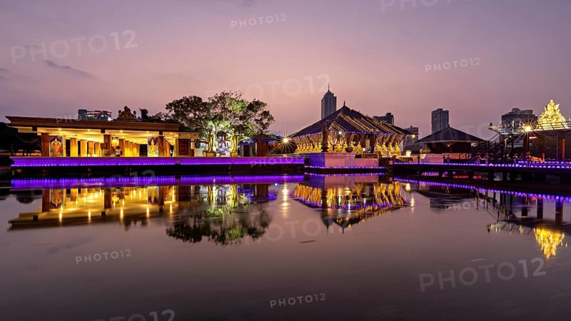 An illuminated temple and city building are reflected in the tranquil lake at dusk, The Seema Malaka Temple in Colombo in Sri Lanka