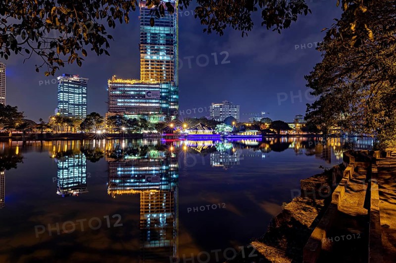 A calm lake reflects an illuminated skyline and urban buildings at night, The Seema Malaka Temple in Colombo in Sri Lanka