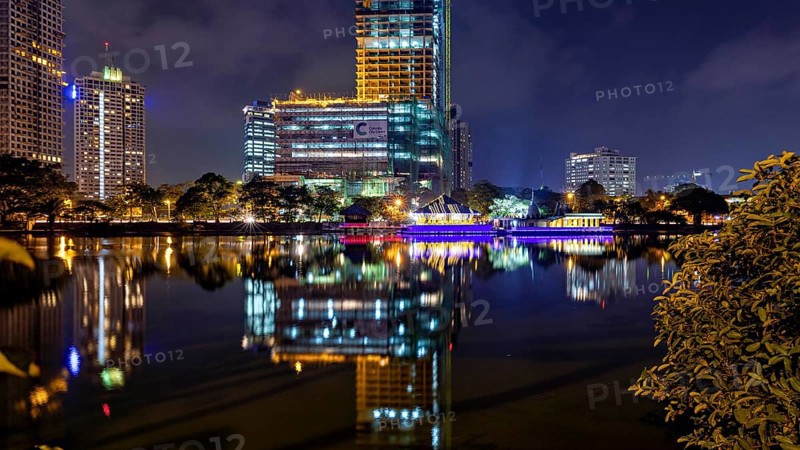 At night, illuminated modern buildings and a temple are reflected in the tranquil lake, The Seema Malaka Temple in Colombo in Sri Lanka