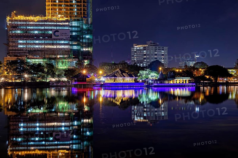 At night, an illuminated temple and urban skyline are reflected in the water, The Seema Malaka Temple in Colombo in Sri Lanka