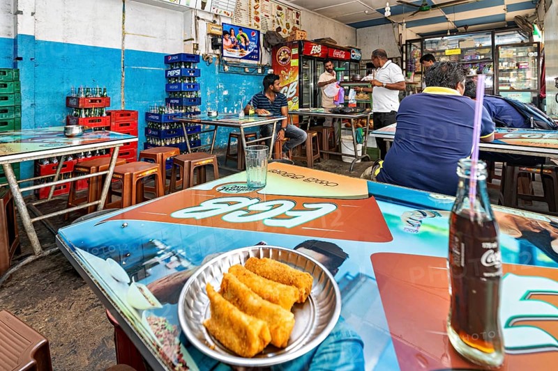 Casual snack with colorful tables and chairs, relaxed atmosphere, food and drinks on the tables, people in a simple restaurant in Colombo in Sri Lanka