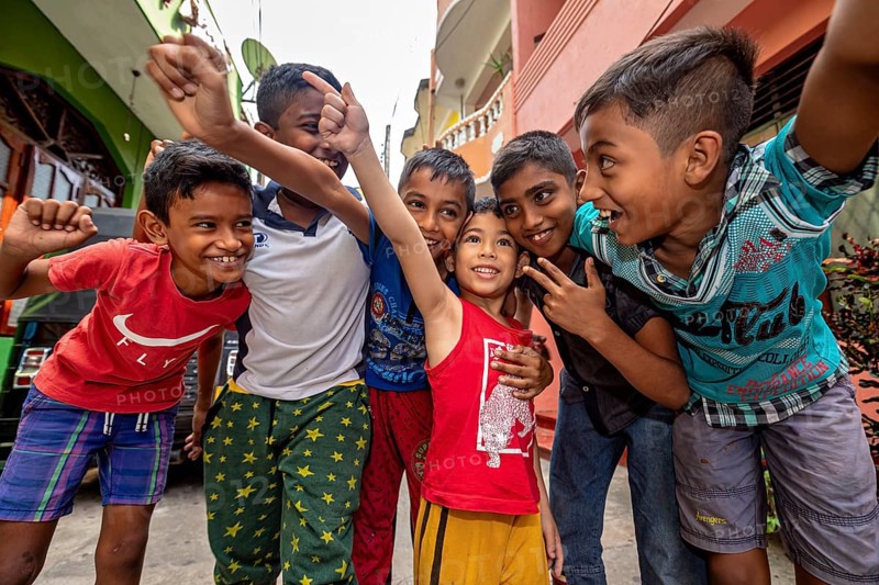 Six laughing and friendly children pose together on a street
