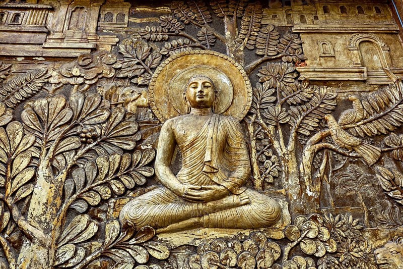 Relief depiction of Buddha in meditation surrounded by plants and architectural details, statues of gods in the temples of Colombo in Sri Lanka