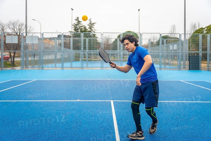 Athlete wearing athletic clothing using a paddle to hit a pickleball during an intense match, demonstrating skill and agility on the brightly colored blue court