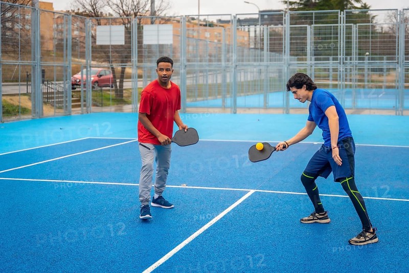 Two men intensely competing in pickleball on a vibrant blue outdoor court, focused and athletic as they rally with paddles and ball in a dynamic, energetic match