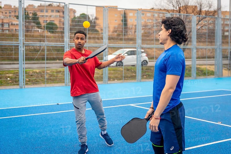 Young men enjoying a game of pickleball, one hitting the ball with a paddle on a vibrant blue court, embodying an active lifestyle and camaraderie in an outdoor setting