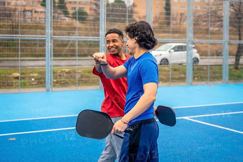 Two diverse male athletes fist bumping on an outdoor blue pickleball court, symbolizing collaboration, camaraderie, and team spirit after a game or practice session