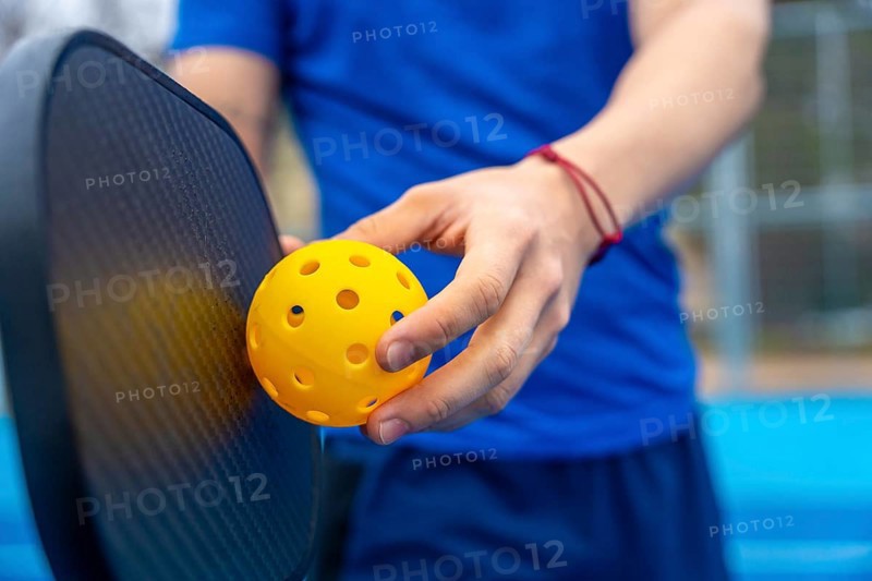Hands holding a yellow pickleball and paddle on an outdoor court, poised to serve or dinkclose up capturing active lifestyle, sport, leisure, and summer fitness readiness